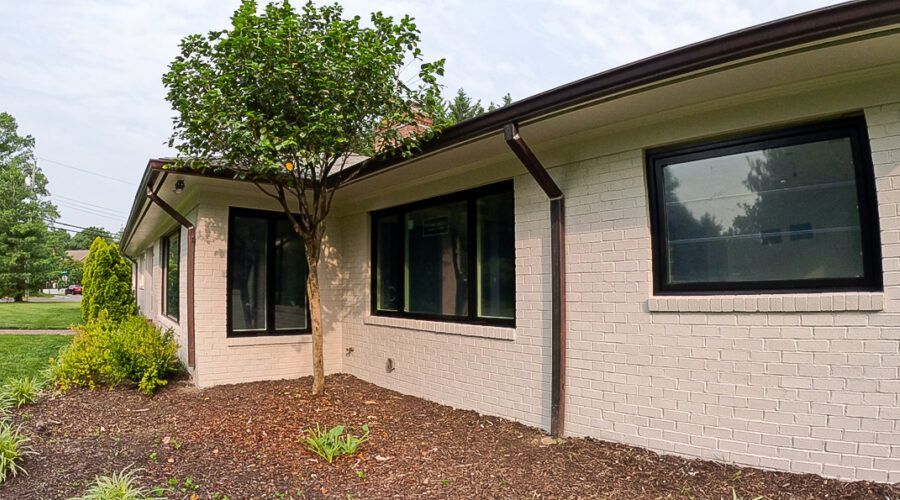 Single-story brick house exterior with large black-trimmed windows and a landscaped front entry.