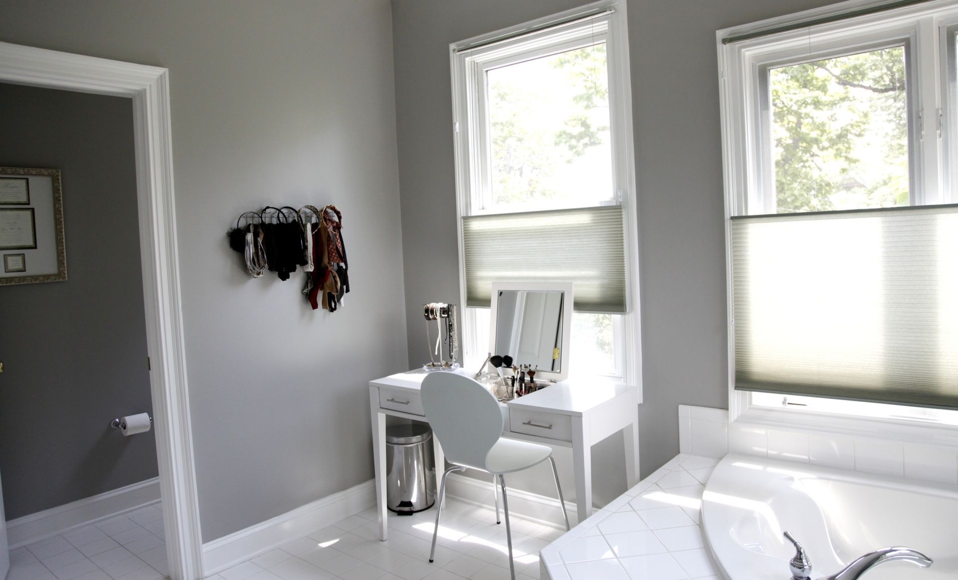 Bright white bedroom with desk, chair, wall hooks, and two sunlit windows