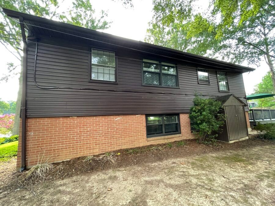 Two-story house with dark siding, brick lower half, and a small covered entrance.