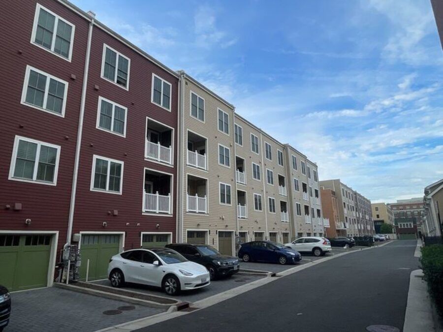 Apartment buildings and parked cars along a quiet residential street under a blue sky.