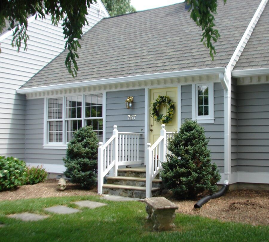 Gray house entrance with white railings, stone steps, and a green wreath on the front door.