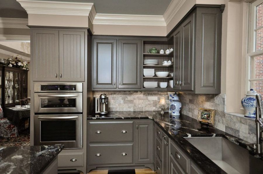 Modern kitchen with gray cabinets, black granite counters, built-in oven, and glass-front shelves