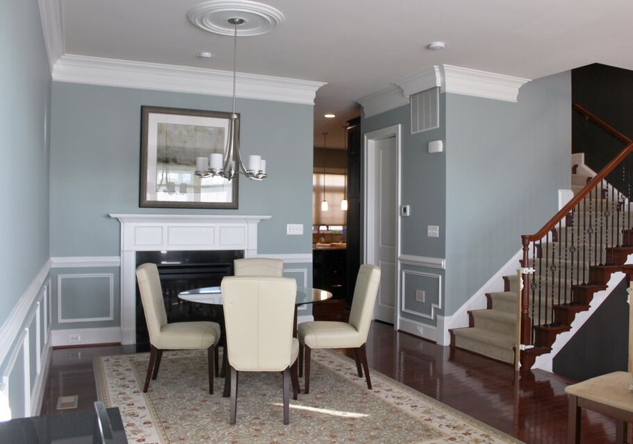 Dining room with beige chairs, white fireplace, gray walls, and staircase in a home interior.