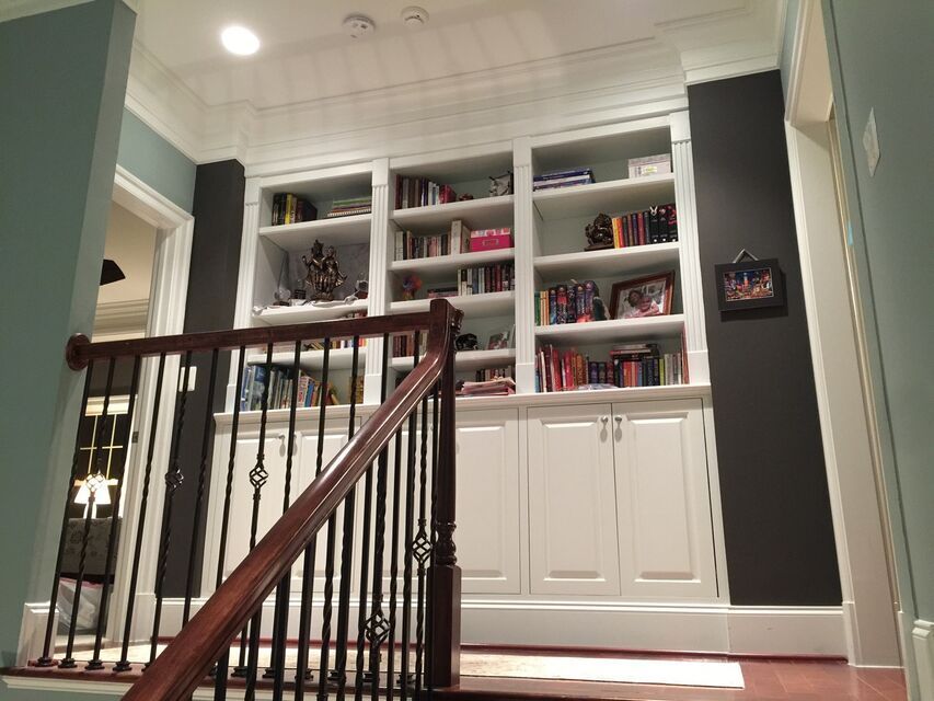 Staircase with dark wood railing leading to built-in white bookshelves filled with books and decor