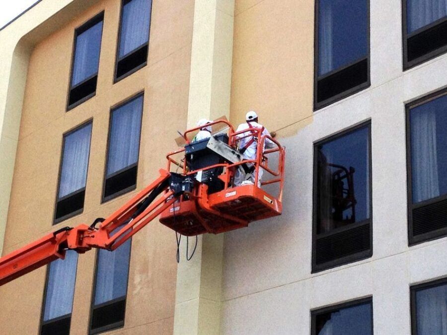 Workers in a red lift inspecting a beige building’s windows
