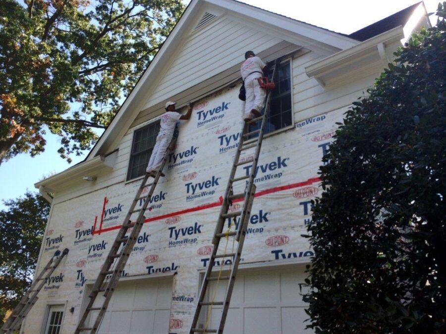 Worker on a ladder installing Tyvek house wrap on a two-story home exterior.