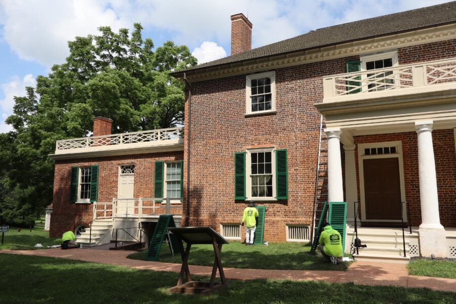 Historic brick house with white columns, green shutters, and lawn mowers on the front lawn