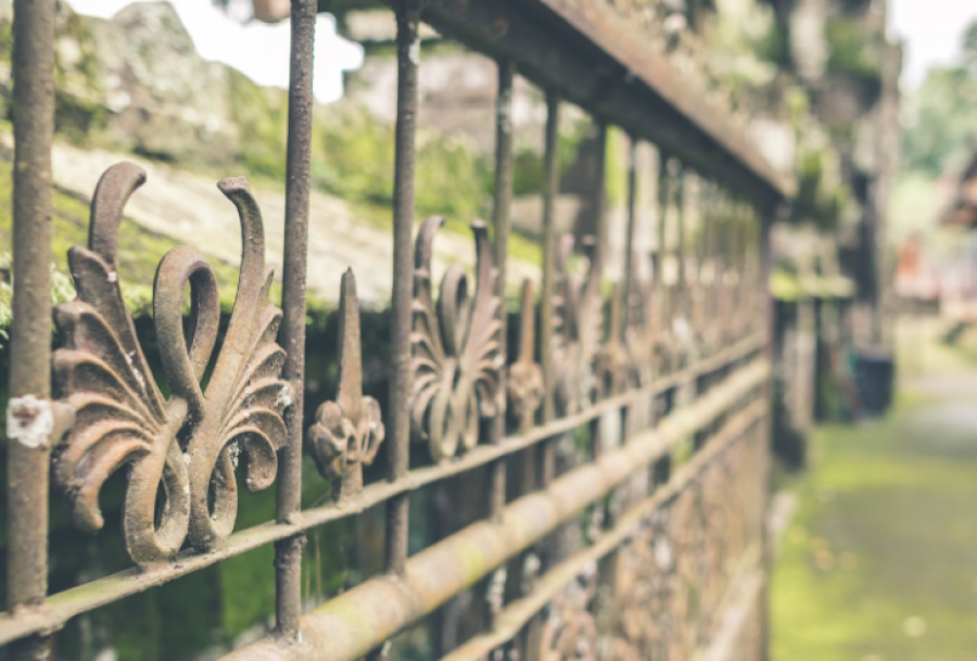 Decorative wrought-iron fence with ornate leaves, stretching along a blurred garden path