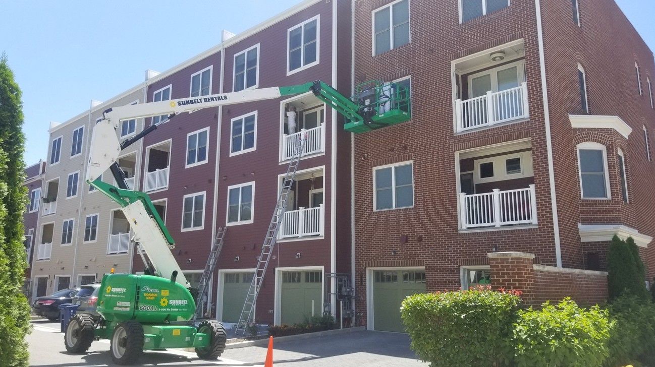 Worker in green lift repairing windows on a red brick apartment building