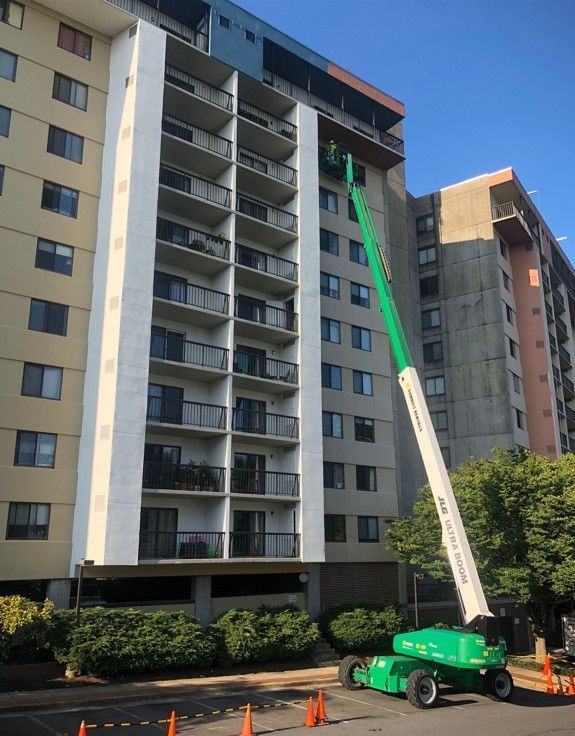 Boom lift reaching up the side of an apartment building during exterior maintenance