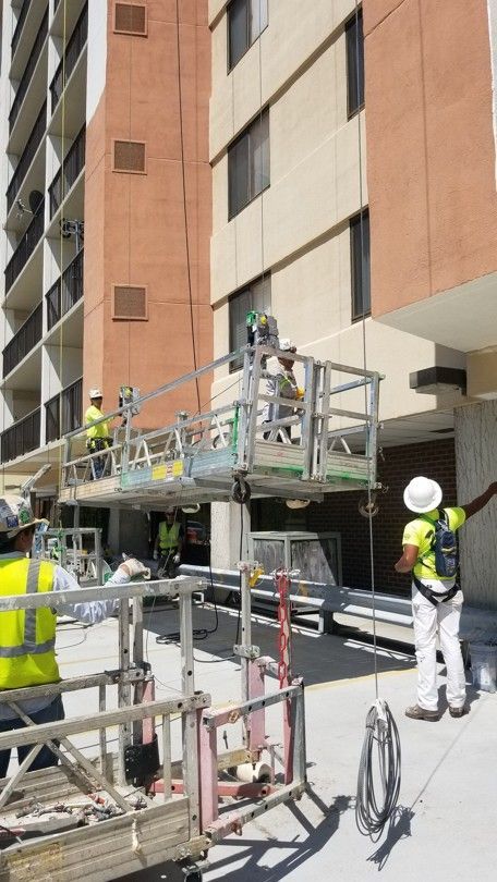 Workers on a lift repairing a tall apartment building exterior, with safety gear and scaffolding below