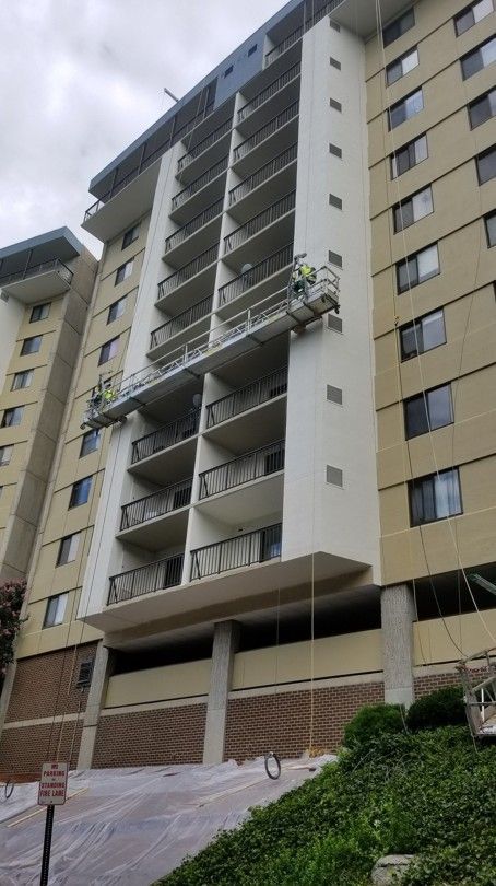 Tall beige apartment building with balconies and a sloped driveway below