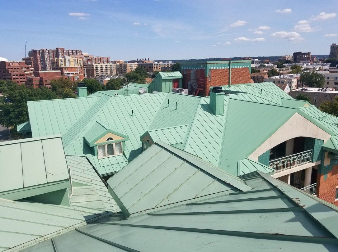 Rooftop with green metal roofs overlooking a city skyline under a clear blue sky