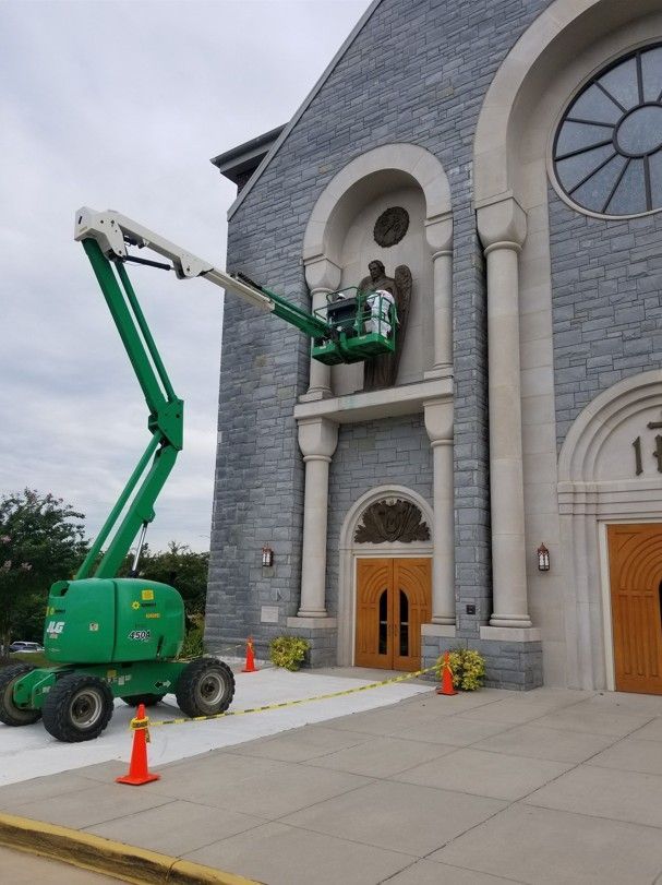 Worker in a green lift replacing a light on a church facade