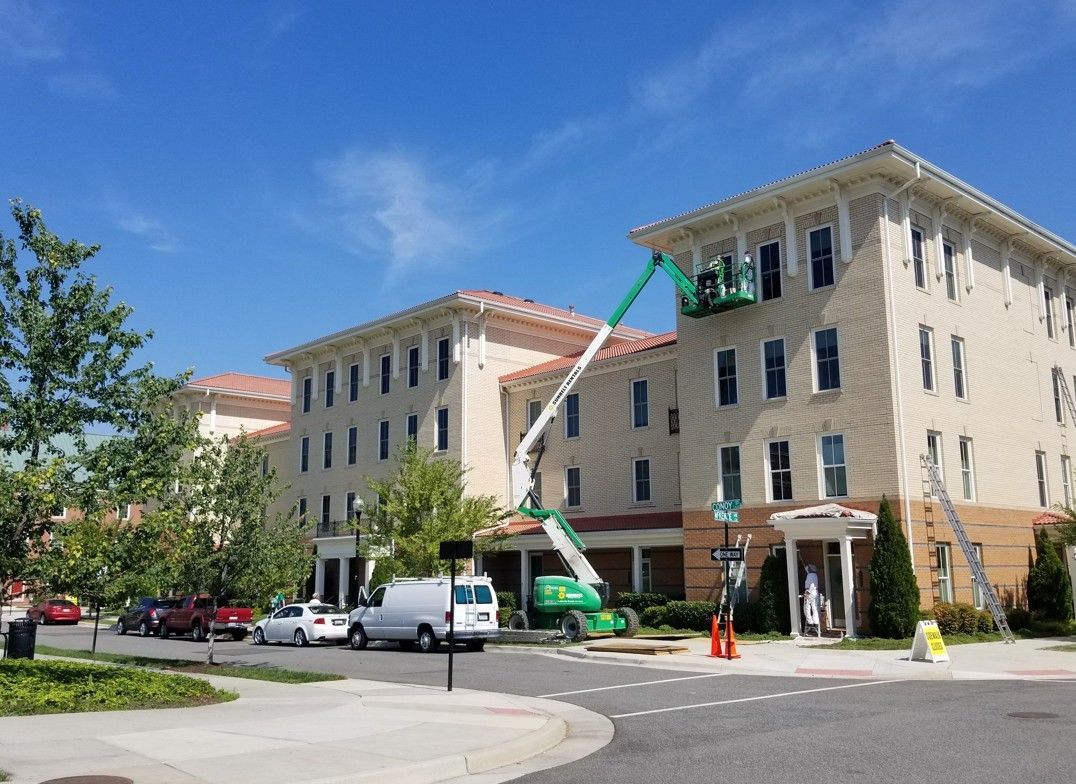 Green lift truck outside a beige building, raising a worker to the upper windows.