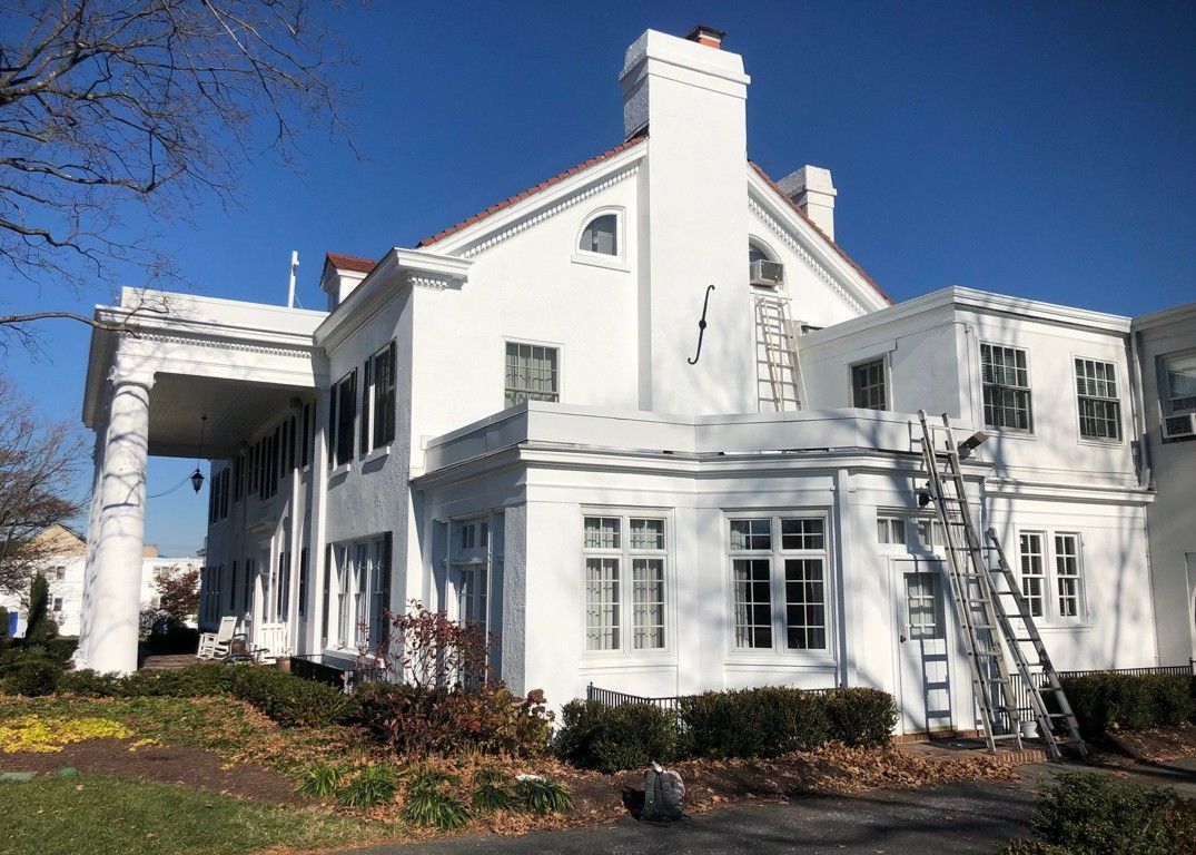 White two-story house with ladders on the side, seen from the yard on a clear day.