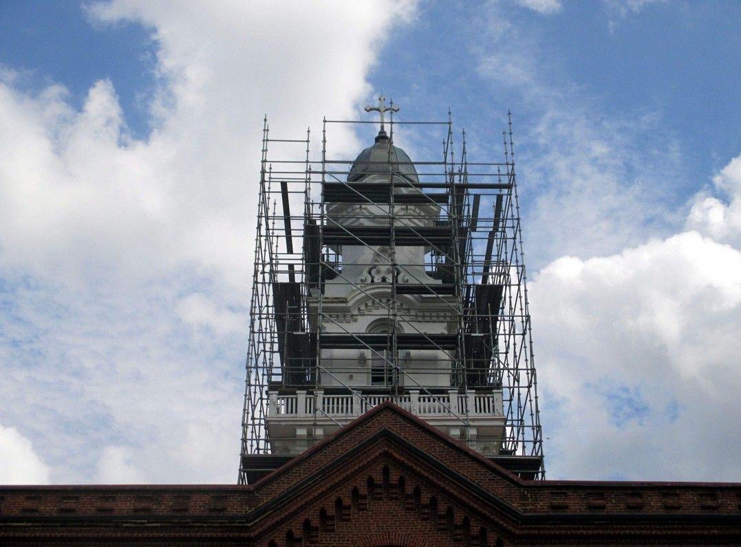Clock tower under scaffolding against a cloudy blue sky, above a brick roofline