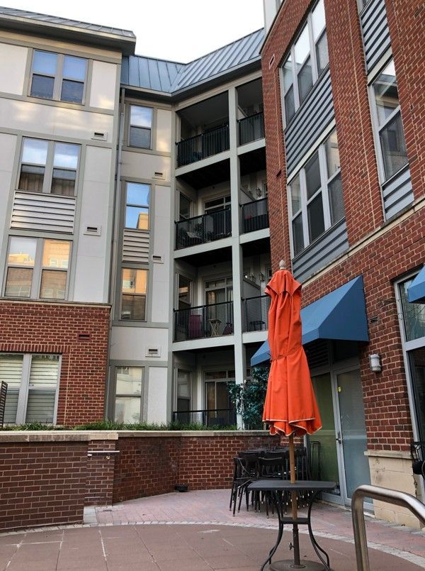 Courtyard between brick apartment buildings with a closed orange patio umbrella and tables