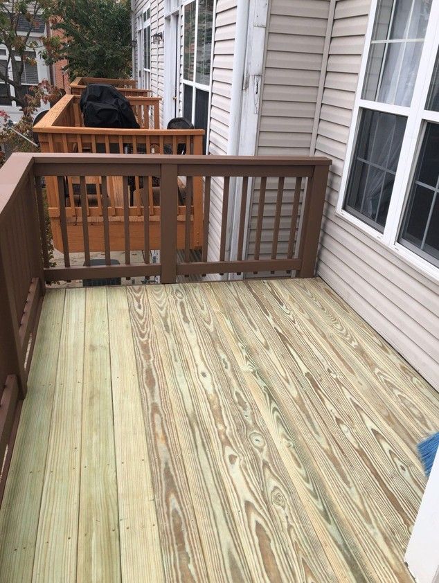 Wooden apartment balcony with railing, light deck boards, and a grill covered near the far end.