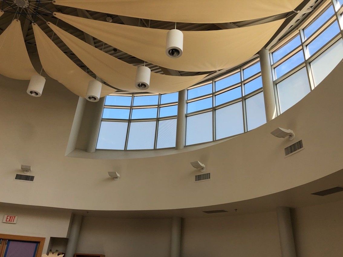 Curved indoor atrium ceiling with skylights, hanging lights, and beige fabric panels