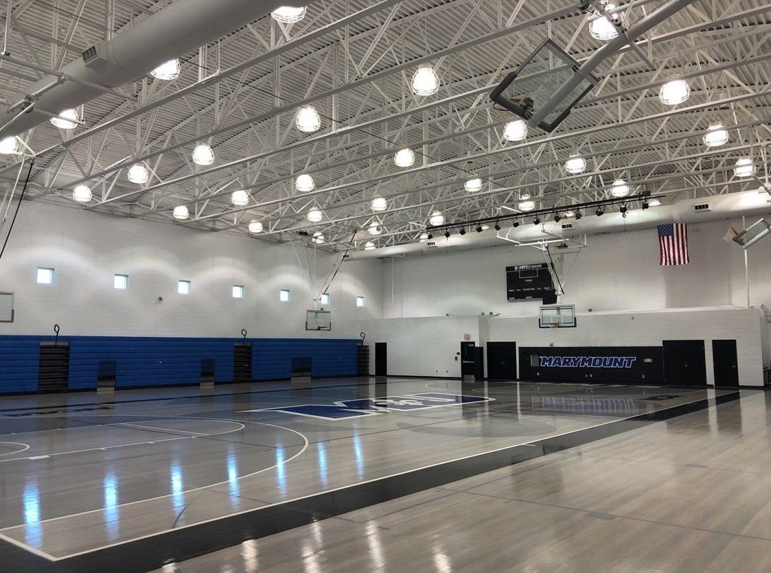 Empty indoor gymnasium with blue bleachers, polished court, and bright ceiling lights