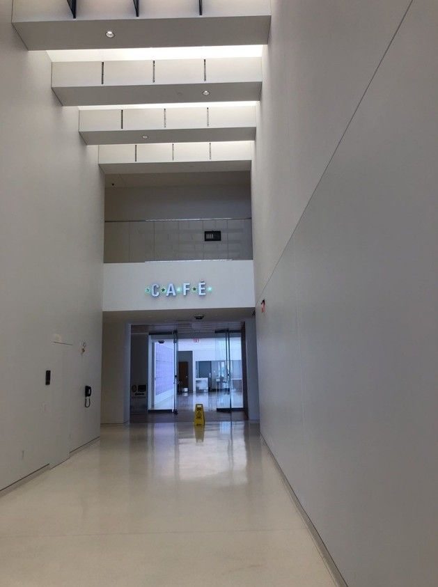 Empty modern lobby corridor with white walls, skylights, glossy floor, and glass doors at the far end