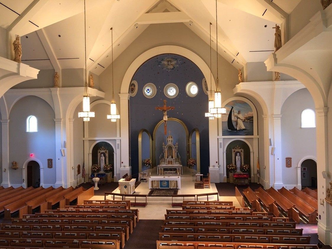 Church sanctuary interior with pews, altar, arched windows, and hanging pendant lights