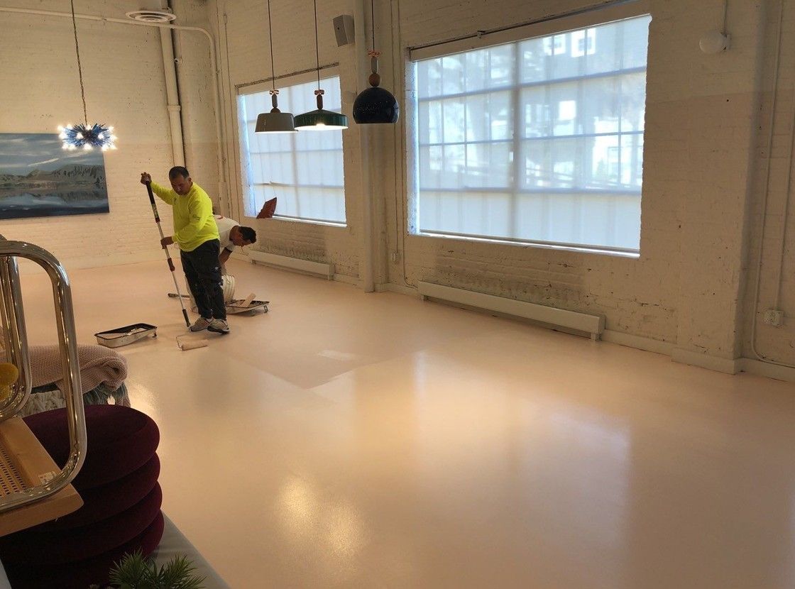 Worker buffing a glossy floor in a bright, empty room with large windows.