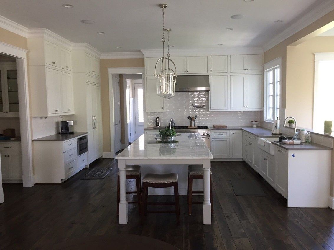 Bright white kitchen with island, dark wood floors, pendant lights, and sink by the window