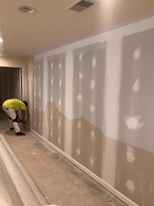 Worker mudding drywall in a hallway with white patch marks on the walls