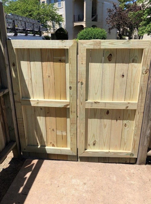 Wooden garden gate with two panels and a latch, set in a sunny backyard patio.
