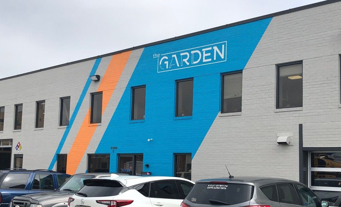 Commercial building with blue and orange facade accents and a “GARDEN” sign above parked cars.