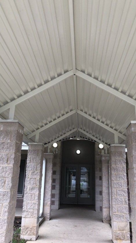 Covered walkway with white vaulted ceiling, brick pillars, and a dark entrance at the end