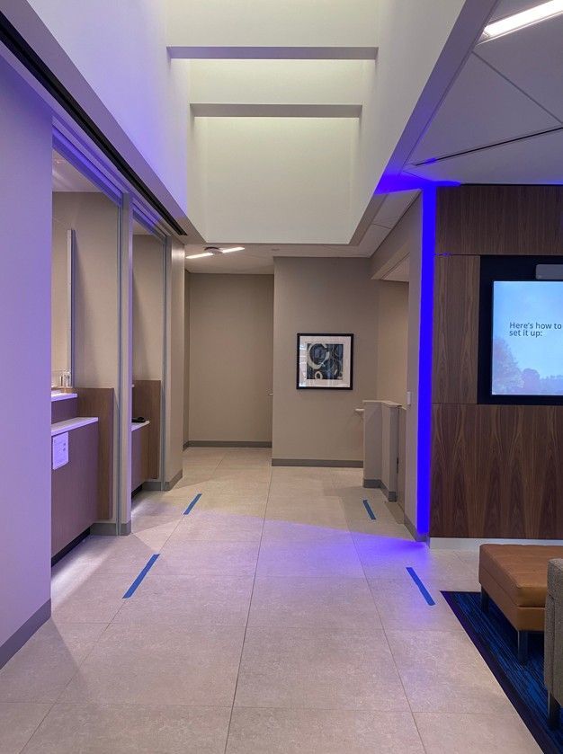 Modern hotel hallway with blue accent lighting, beige tile floor, and a framed artwork on the far wall