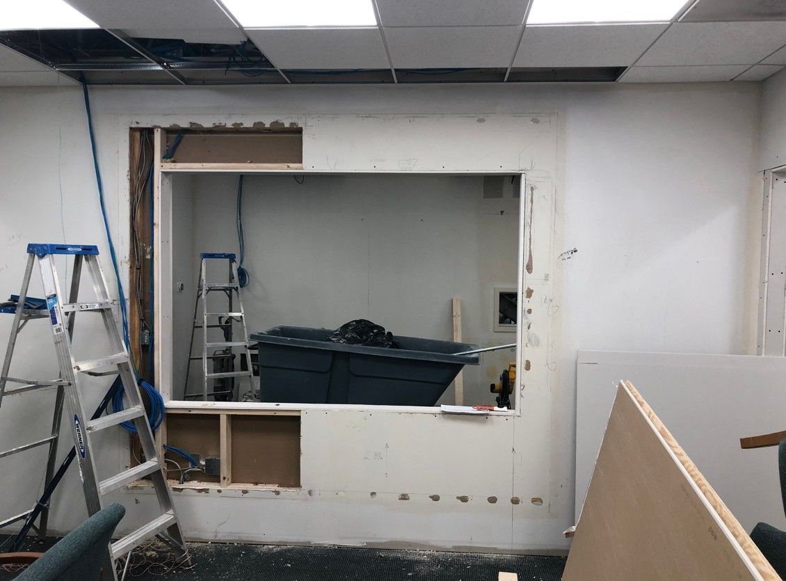 Partially demolished wall with large opening in an unfinished room, ladders and construction materials visible.