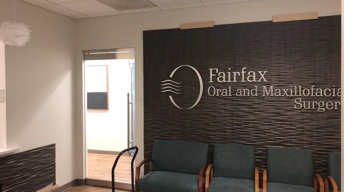 Waiting room with teal chairs and a wall sign for Fairfax Oral and Maxillofacial Surgery