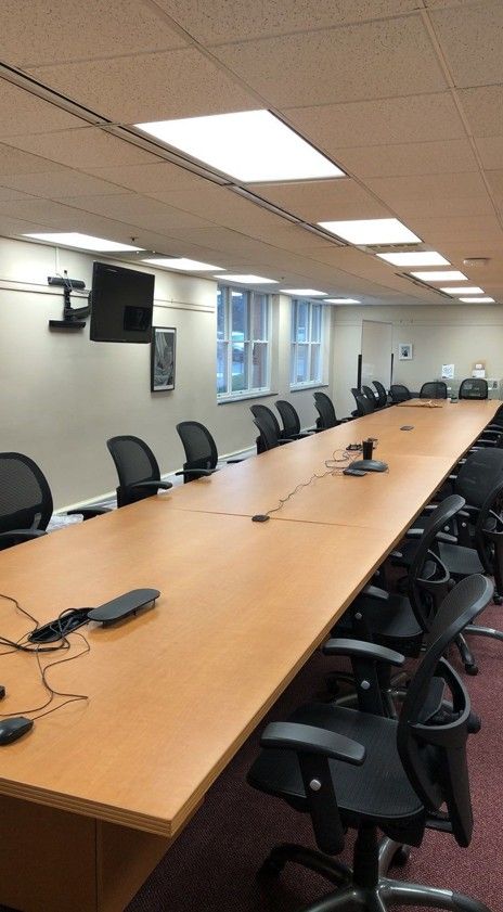 Empty conference room with a long wooden table, black office chairs, and wall windows under fluorescent lights