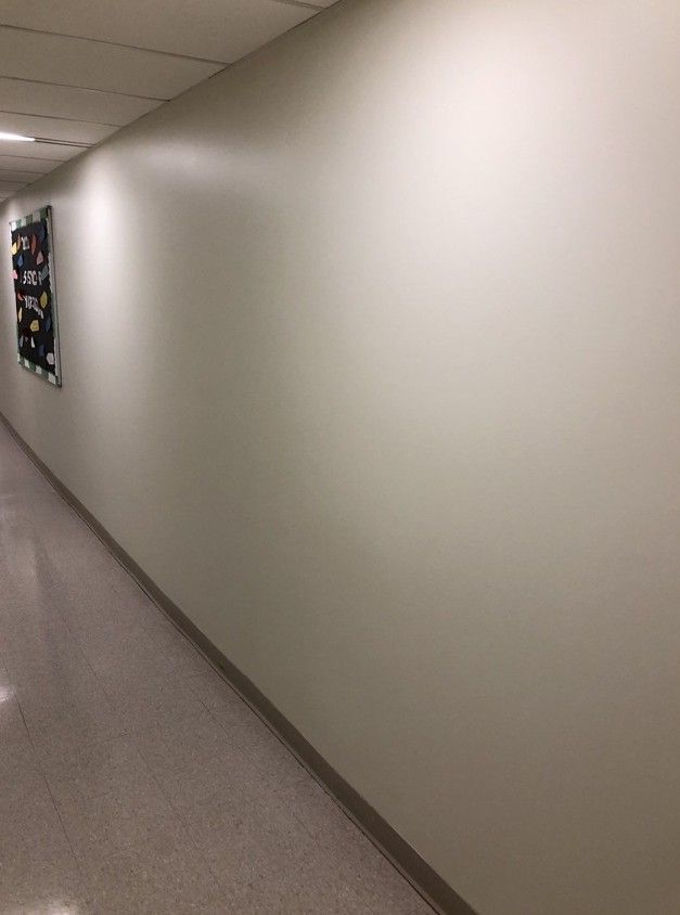 Empty beige hallway with a framed wall hanging on the left.