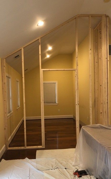 Partially renovated room with slanted ceiling, exposed framing, and plastic-covered furniture.