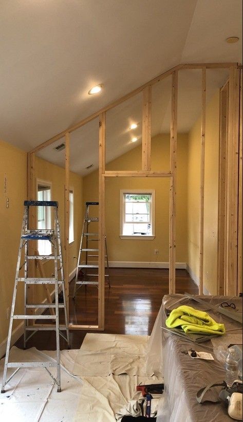 Interior room under renovation with exposed wooden framing, ladder, and plastic drop cloths on the floor.