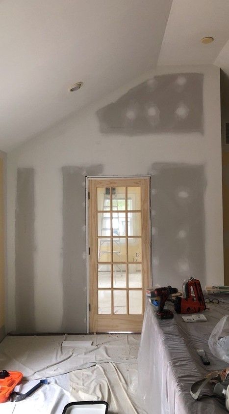 Interior room under renovation with drywall patches, a sloped ceiling, and a glass door centered on the back wall