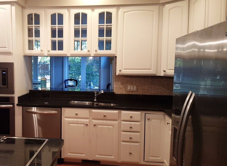 Bright white kitchen with black countertops, stainless dishwasher, and large window above the sink.
