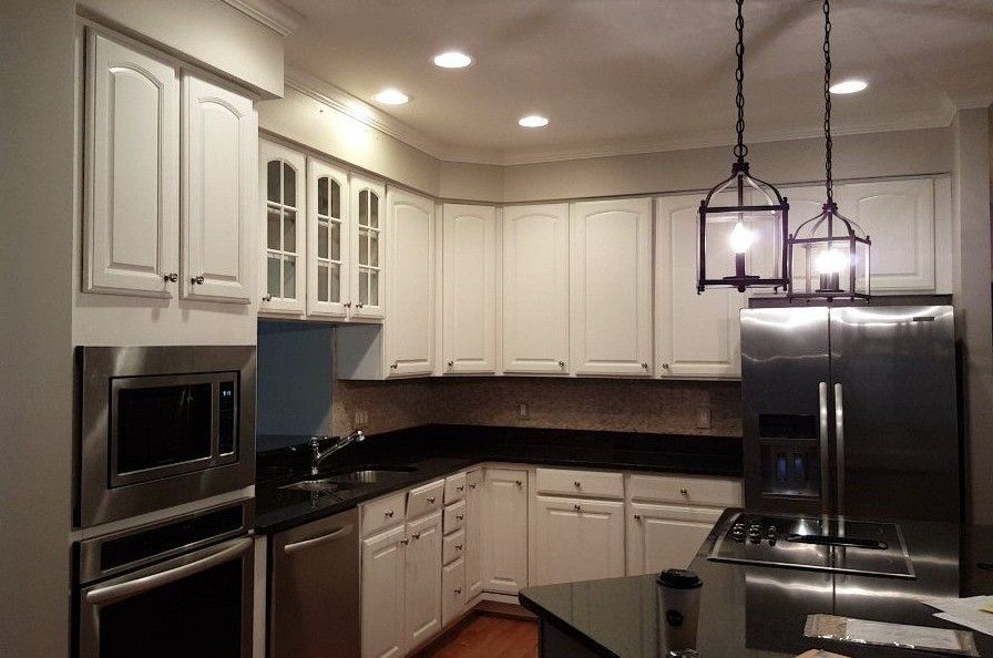 Modern kitchen with white cabinets, black countertops, stainless appliances, and hanging pendant lights