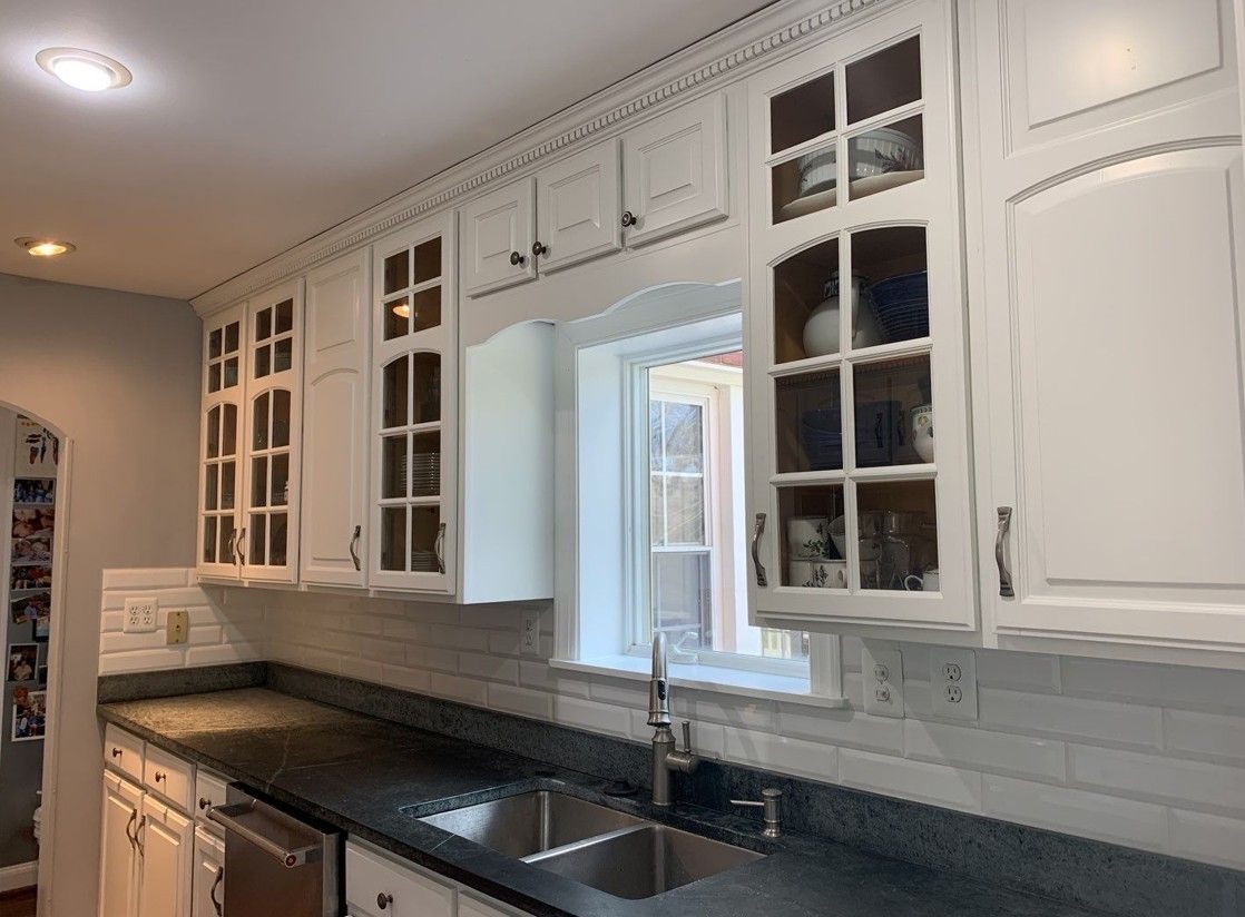 Bright kitchen with white cabinets, dark countertops, and a black sink under a pass-through window.