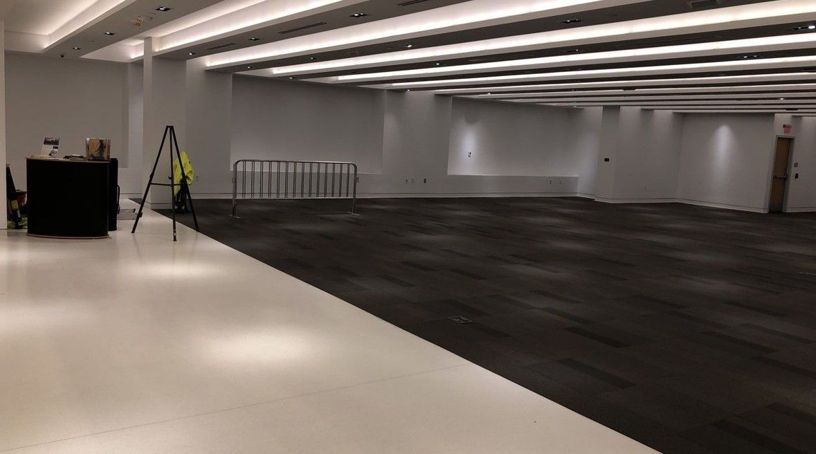 Empty indoor hall with white floor, dark central carpet, and a small ladder near the back wall