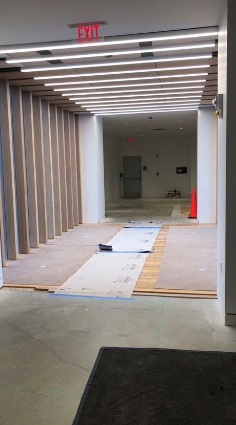 Indoor hallway under renovation with exposed floor coverings, ceiling lights, and a cone at the far end