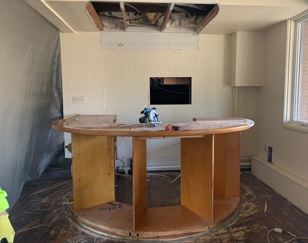 Partially renovated room with a central wooden counter, plastic-covered walls, and exposed ceiling