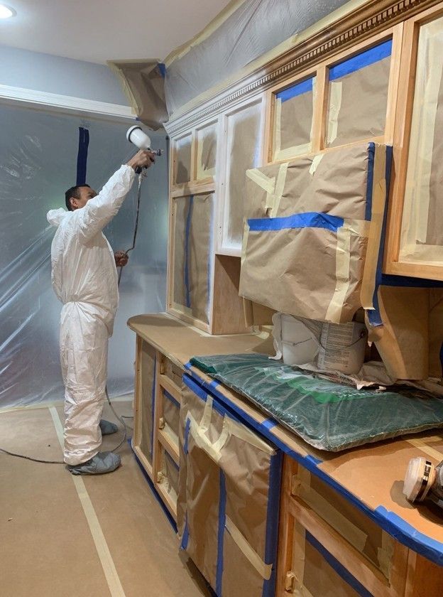 Worker in white protective suit spray-painting a room while furniture is masked with paper and tape