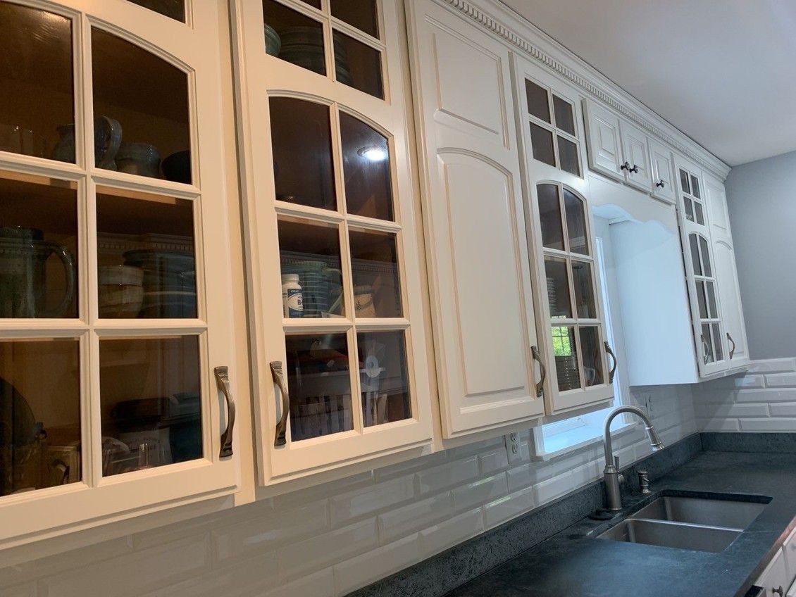 White kitchen with glass-front cabinets, subway tile backsplash, and a black countertop with sink.