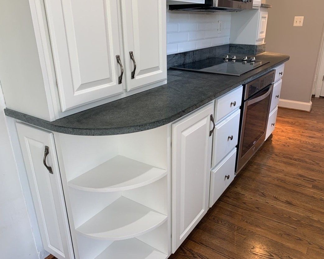 Modern kitchen with white cabinets, gray countertop, stove, and hardwood floor